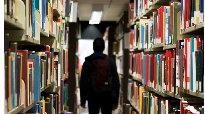 A student walks through rows of books at a library