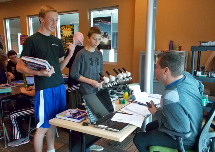 Compass charter school students talk to their professor in their classroom