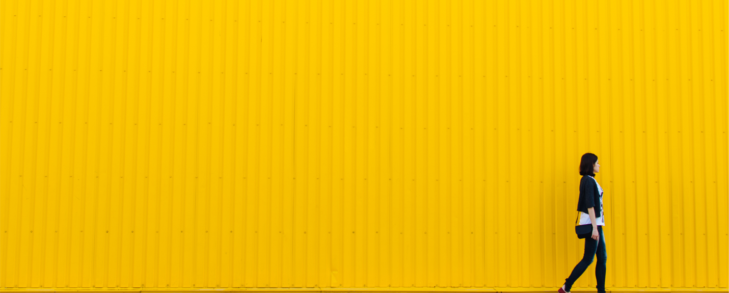 A woman walks in front of a bright yellow wall