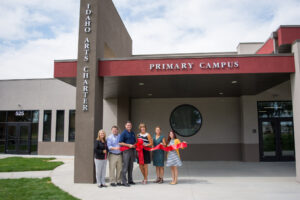 The Bluum team stands in front of the entrance to Idaho Arts Charter School's Primary Campus holding a red ribbon