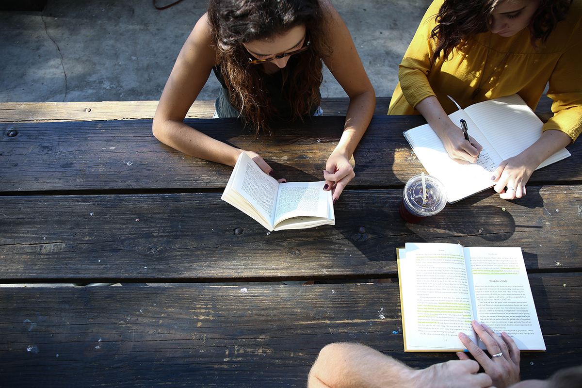 Two students write in notebooks outside