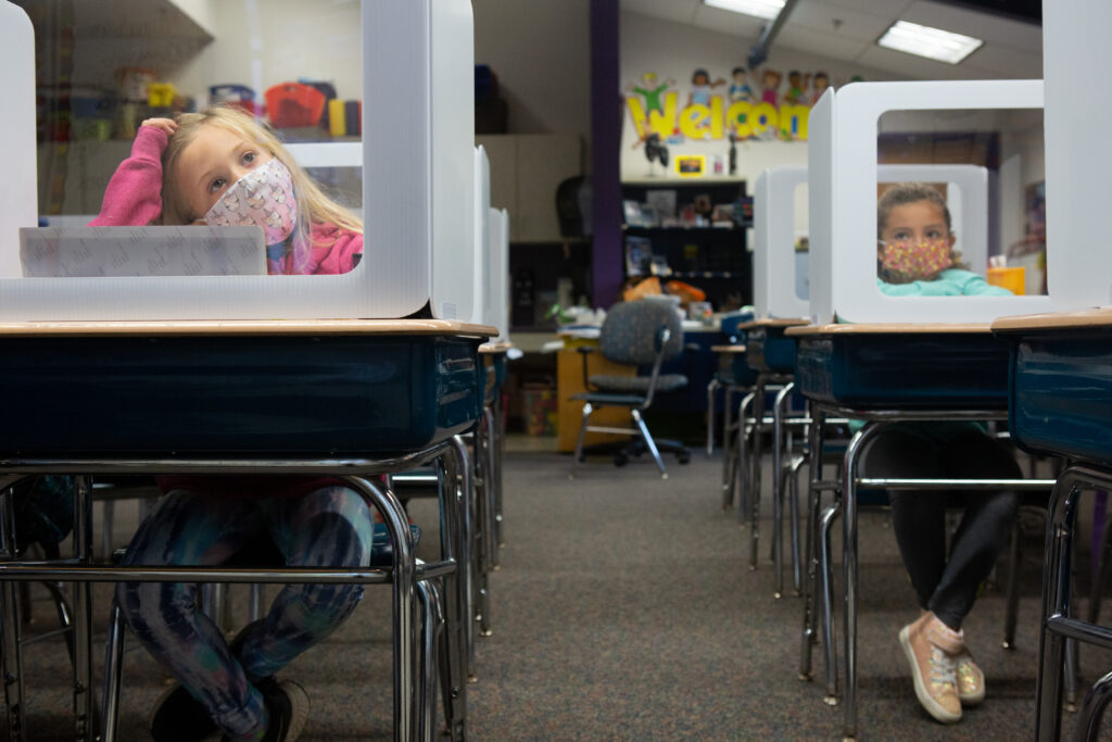 Two students sit at their desks behind plexiglass