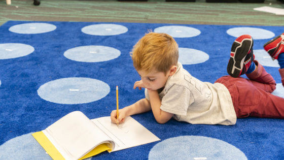 A student lays down on a blue carpet writing