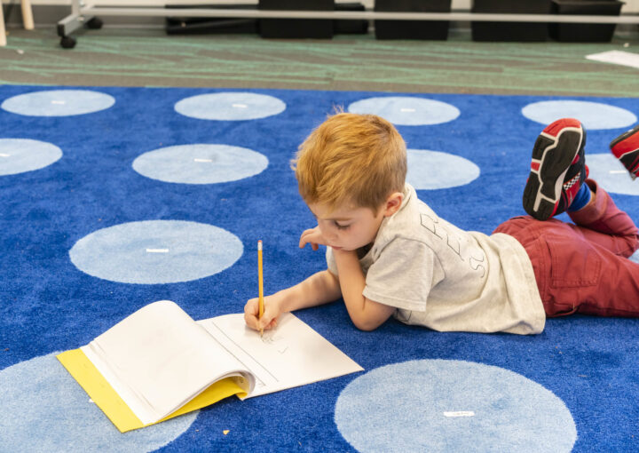 A student lays down on a blue carpet writing