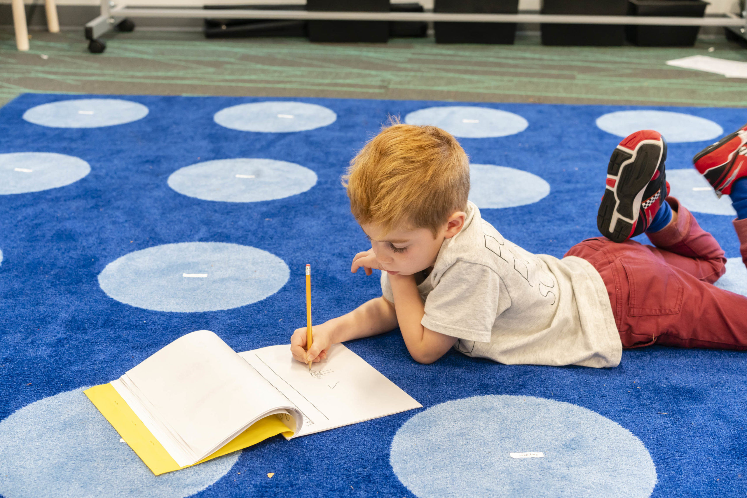 A student lays down on a blue carpet writing