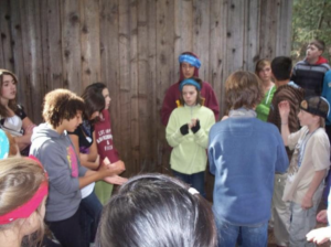 Maura Romano stands with 7th and 8th grade students completing “the wall,” one of the team building activities up at the McCall based ropes course. 