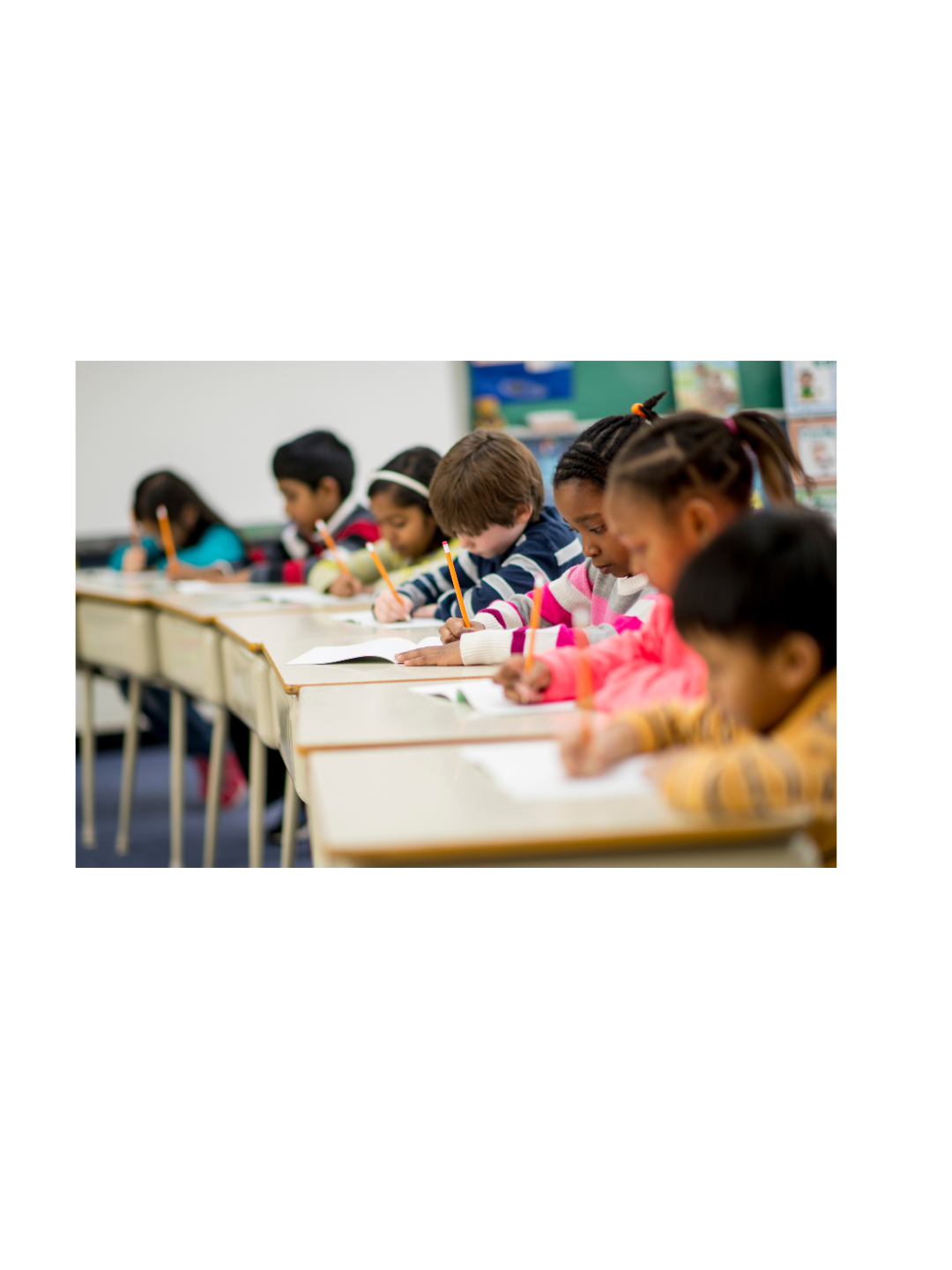Elementary school students seated at classroom desks, writing in notebooks and completing schoolwork.